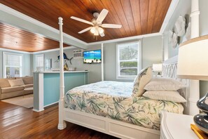Un dormitorio con cama, ventilador de techo, televisor y ventana con persianas.