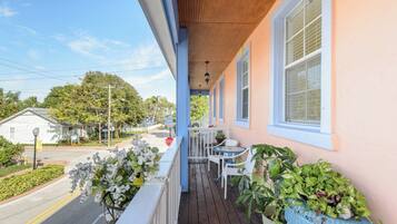 A porch with a table and chairs, potted plants, and a view of the street.