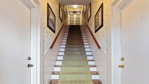 Una escalera con alfombra estampada y escalones de madera que conduce a una puerta con un letrero encima.