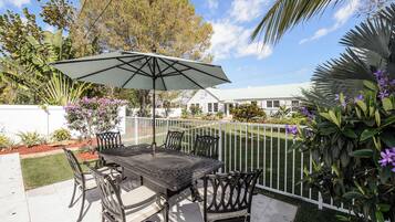 An outdoor patio with a table and chairs, a white fence, and various plants.