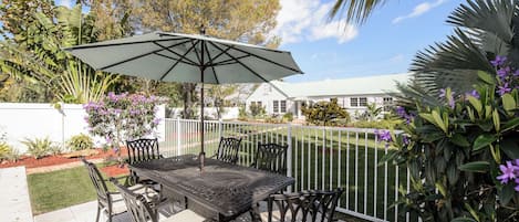 An outdoor patio with a table and chairs, a white fence, and various plants.