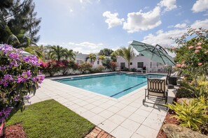 Piscina com deck revestido em azulejos, rodeada por vegetação exuberante e plantas floridas.