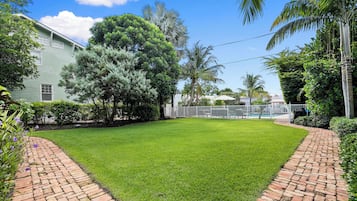 A well-maintained lawn with a brick pathway, surrounded by various trees and a white fence.