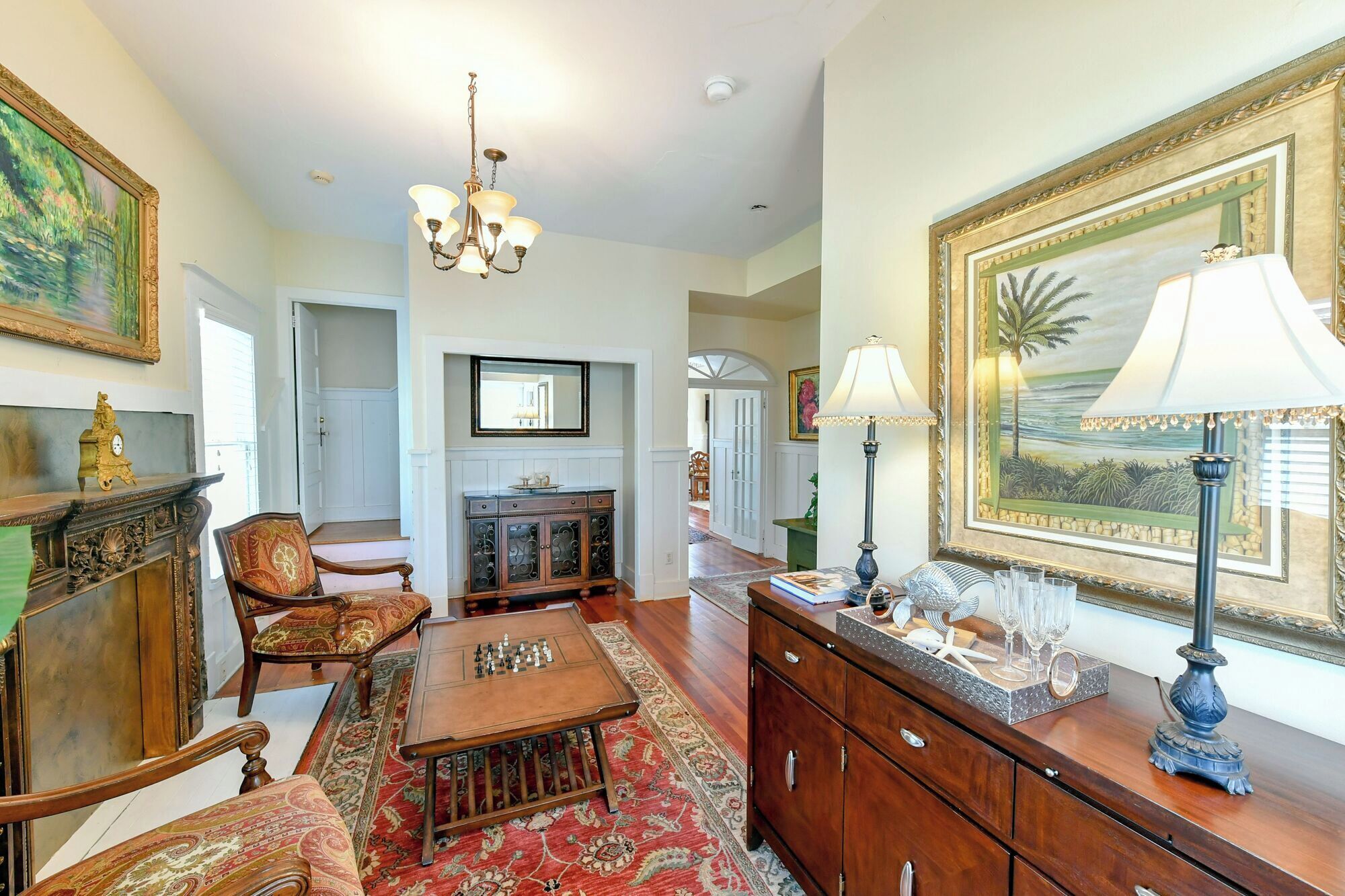 A spacious living room with a fireplace, a chandelier, and a large framed painting.
