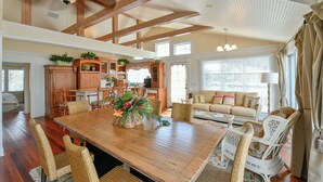 Un comedor amplio con una mesa de madera y sillas de mimbre, una cocina con armarios de madera, y una sala de estar con sofá y cortinas.