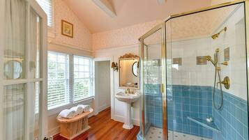 A bathroom with a glass shower enclosure, a pedestal sink, and a vanity with towels.