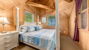 A wooden-paneled bedroom with a four-poster bed, a nightstand, and a window with a view of greenery.