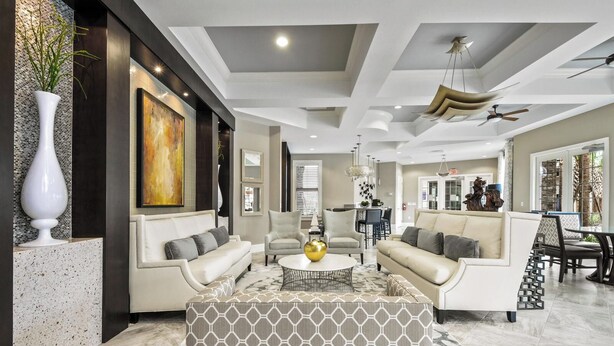 A modern living room with a sofa, armchairs, and a coffee table. There is a painting on the wall and a vase with plants. - 7655 Oakmoss Loop (Davenport)