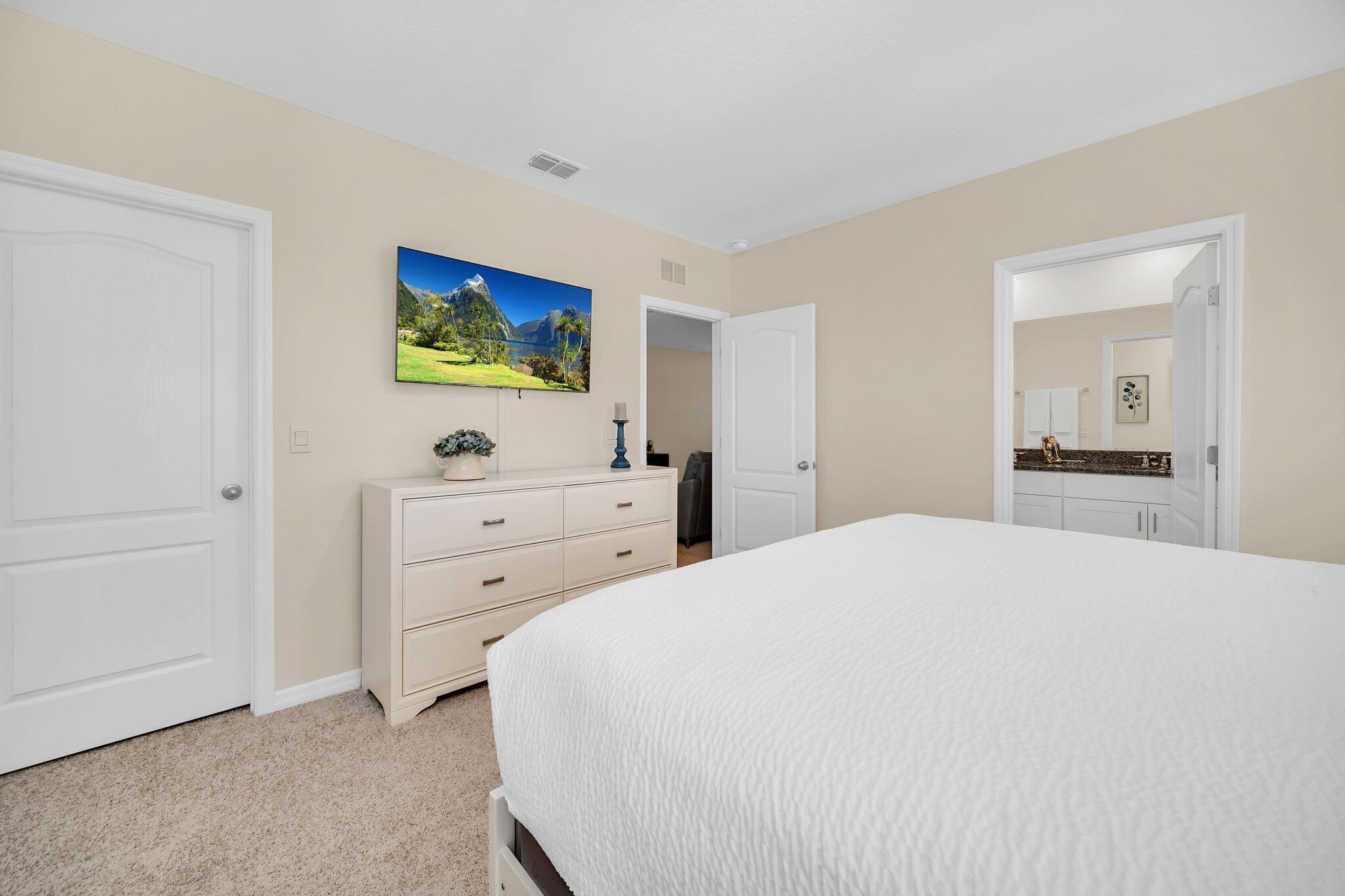 A bedroom with a large bed, a dresser, a painting, and a door leading to a bathroom.