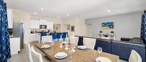 A modern kitchen with white cabinets, a stainless steel refrigerator, and a dining area with a wooden table set for four.