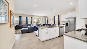 A modern kitchen with white cabinets, a stainless steel refrigerator, and a granite countertop. - 7655 Oakmoss Loop (Davenport)