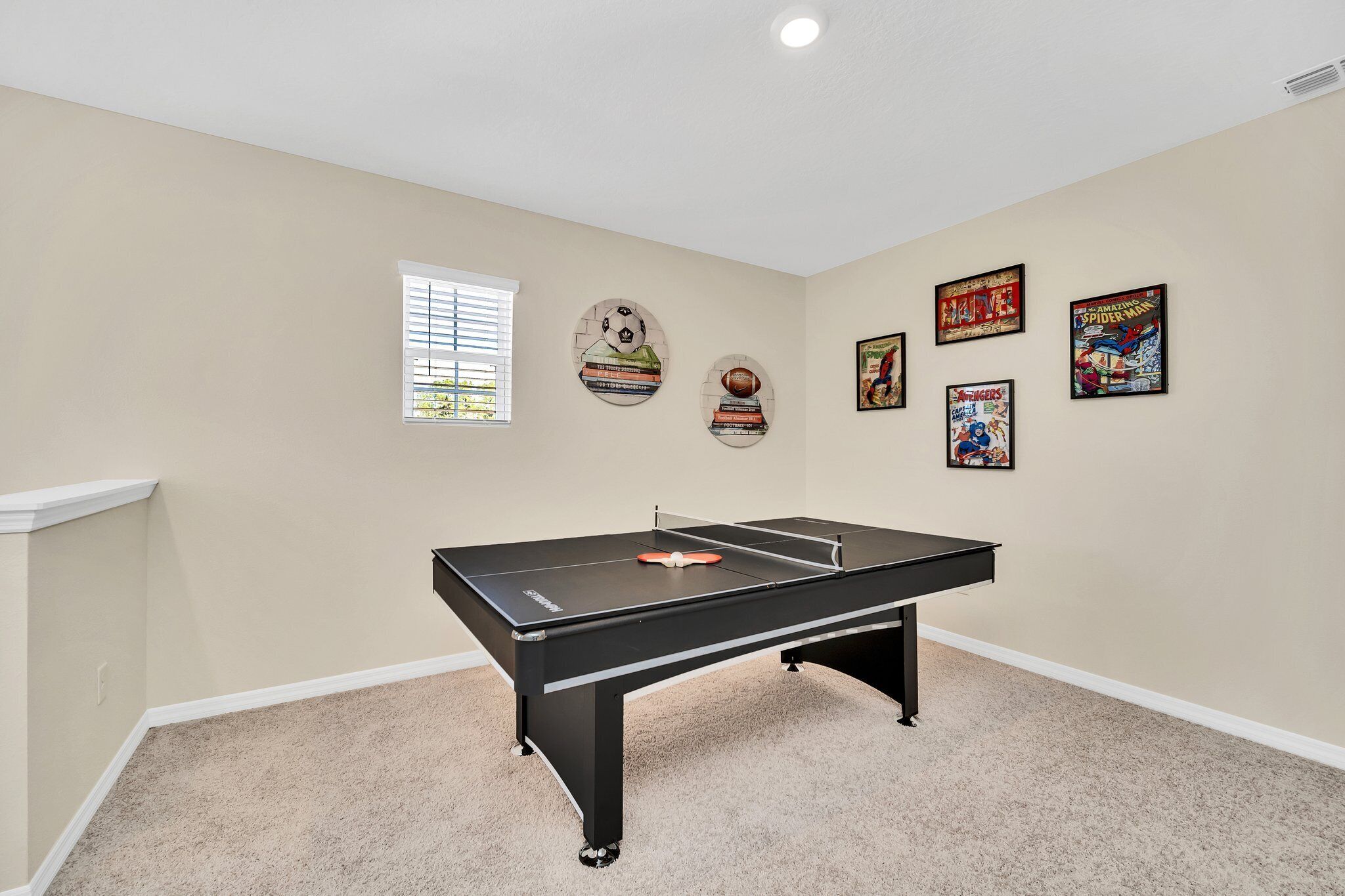 A room with a pool table, beige walls, and sports-themed wall art.