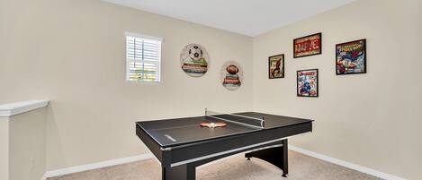 A room with a pool table, beige walls, and sports-themed wall art.