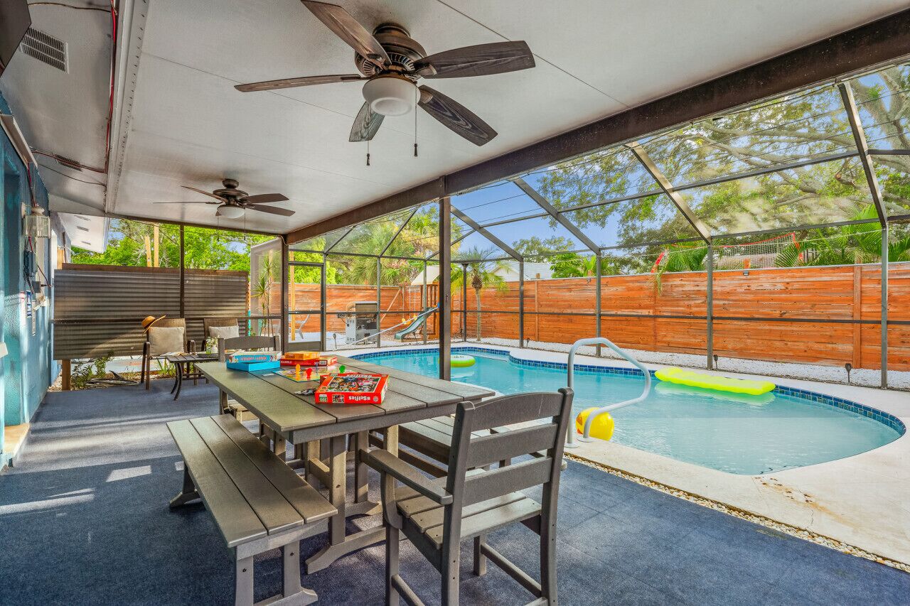 A covered outdoor area with a pool, seating, and a ceiling fan.