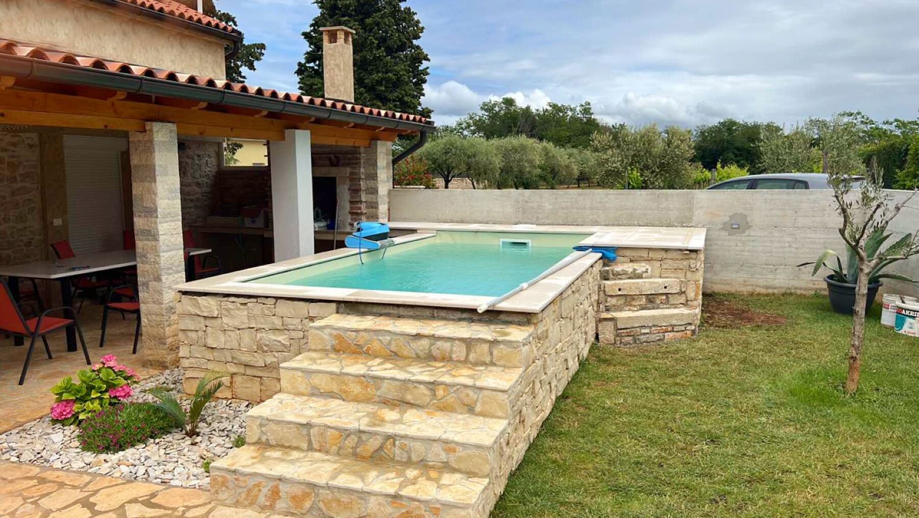 Ein Pool mit Steinabstufungen, eine überdachte Terrasse und eine kleine Gartenanlage mit Blumen.