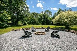 Relax in a serene outdoor setting with Adirondack chairs surrounding a central fire pit.