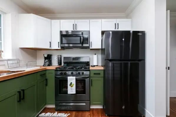 Compact kitchen with a gas stove, refrigerator, and microwave, along with a coffee maker and wooden countertop.