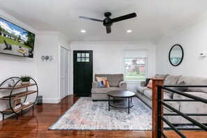 Un salon moderne avec un ventilateur de plafond noir, un canapé gris, une table basse et un tapis à motifs.