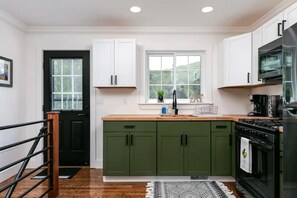 Une cuisine avec des meubles de couleur verte, une cuisinière noire et une fenêtre au-dessus de l’évier.