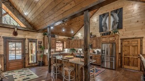 A rustic cabin interior with a large wooden dining table, bar stools, a kitchen area, and a mounted animal head. - Luxury Cabin-Chic getaway w/hot tub, Gated community, River access, Easy drive (Blue Ridge)
