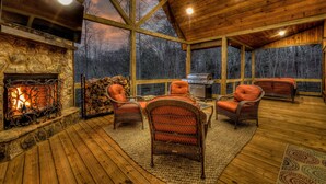A cozy cabin interior with a stone fireplace, wicker furniture, and a large window overlooking a forest. - Luxury Cabin-Chic getaway w/hot tub, Gated community, River access, Easy drive (Blue Ridge)