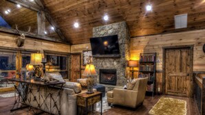 A log cabin interior with a stone fireplace, leather furniture, and a mounted deer head. - Luxury Cabin-Chic getaway w/hot tub, Gated community, River access, Easy drive (Blue Ridge)