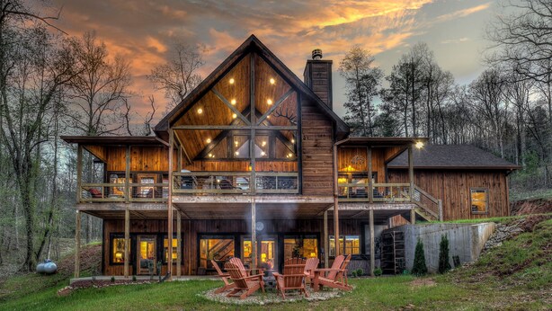 A large wooden cabin with multiple levels, outdoor seating, and a scenic forest backdrop. - Luxury Cabin-Chic getaway w/hot tub, Gated community, River access, Easy drive (Blue Ridge)