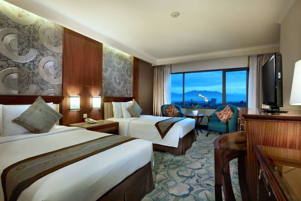 Habitación de hotel con dos camas, televisión, escritorio y vistas a la montaña.