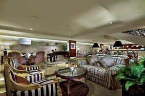 Un hall d'hôtel avec des canapés et des fauteuils à rayures, une table ronde et un écran de télévision.