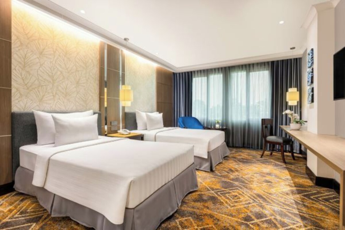 Une chambre d’hôtel avec deux lits, un bureau, une chaise et une grande fenêtre avec des rideaux.
