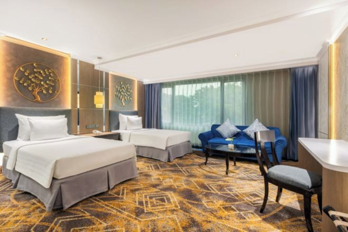 Une chambre d’hôtel avec deux lits, un canapé, un bureau et une grande fenêtre avec des rideaux.