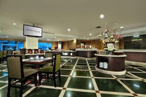 Un hall de hotel con mostrador de recepción, área de descanso y una pantalla grande que muestra el nombre del hotel.