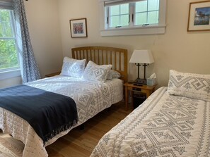 A bedroom with two beds, a wooden headboard, a bedside table with a lamp, and a window with curtains. - Across the street from Acadia and walk to town! (Bar Harbor)