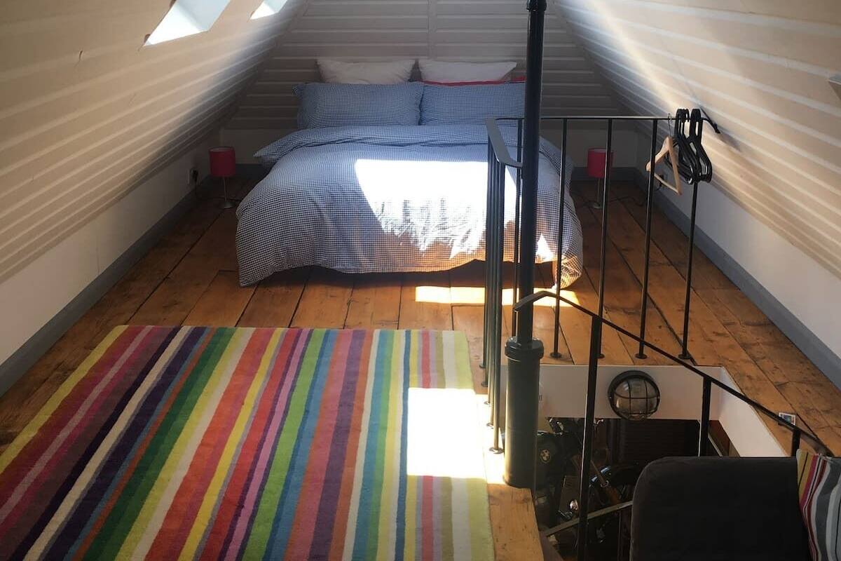 A small, cozy attic bedroom with a sloped ceiling, a bed with checkered bedding, a colorful striped rug, and a black chair.