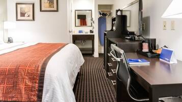 A hotel room with a bed, a desk with a computer, a television, and a bathroom visible through an open door.