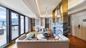 A spacious living room with a large sofa, a round coffee table, and a chandelier. There are large windows offering a view of the outdoors. - Howard Johnson by Wyndham Lake Serenity Hot Springs Xichang (Liangshan Yi)