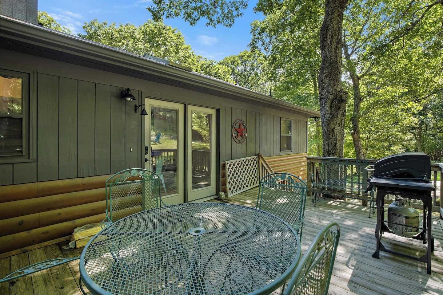 A covered outdoor area with a metal table and chairs, a grill, and a wooden deck.
