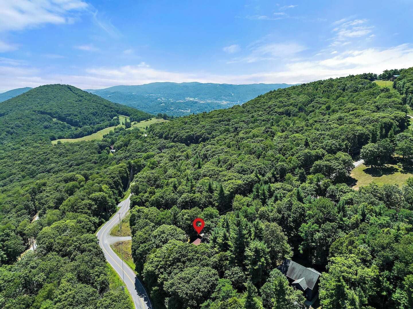 A lush green landscape with a winding road and a red location marker indicating a specific area.