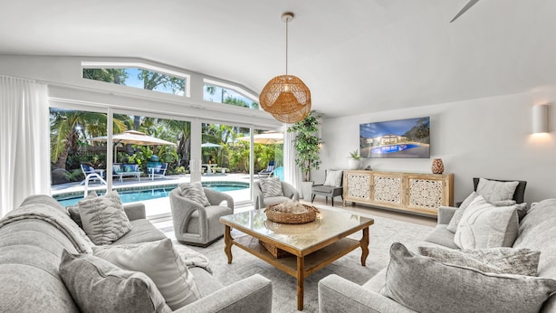 Ein geräumiges Wohnzimmer mit einem großen Glastisch, grauen Sofas und Blick auf einen Swimmingpool.