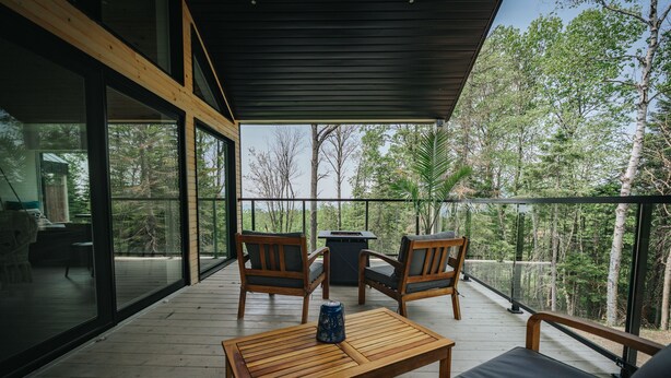 A wooden deck with a table and chairs, overlooking a forested area.