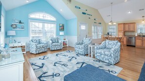 A spacious living room with a high ceiling, nautical-themed decor, and a view of the kitchen. - Bright and sunny family friendly cottage, 2 minutes to beach, Sound view sunsets (Kill Devil Hills)