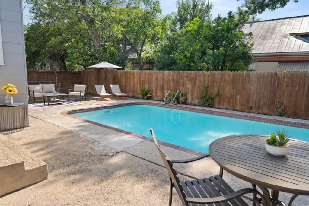 A backyard with a swimming pool, a wooden deck, and a fenced area.