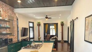 Una cocina moderna con una isla central, gabinetes verdes y una pared de ladrillo decorativa.