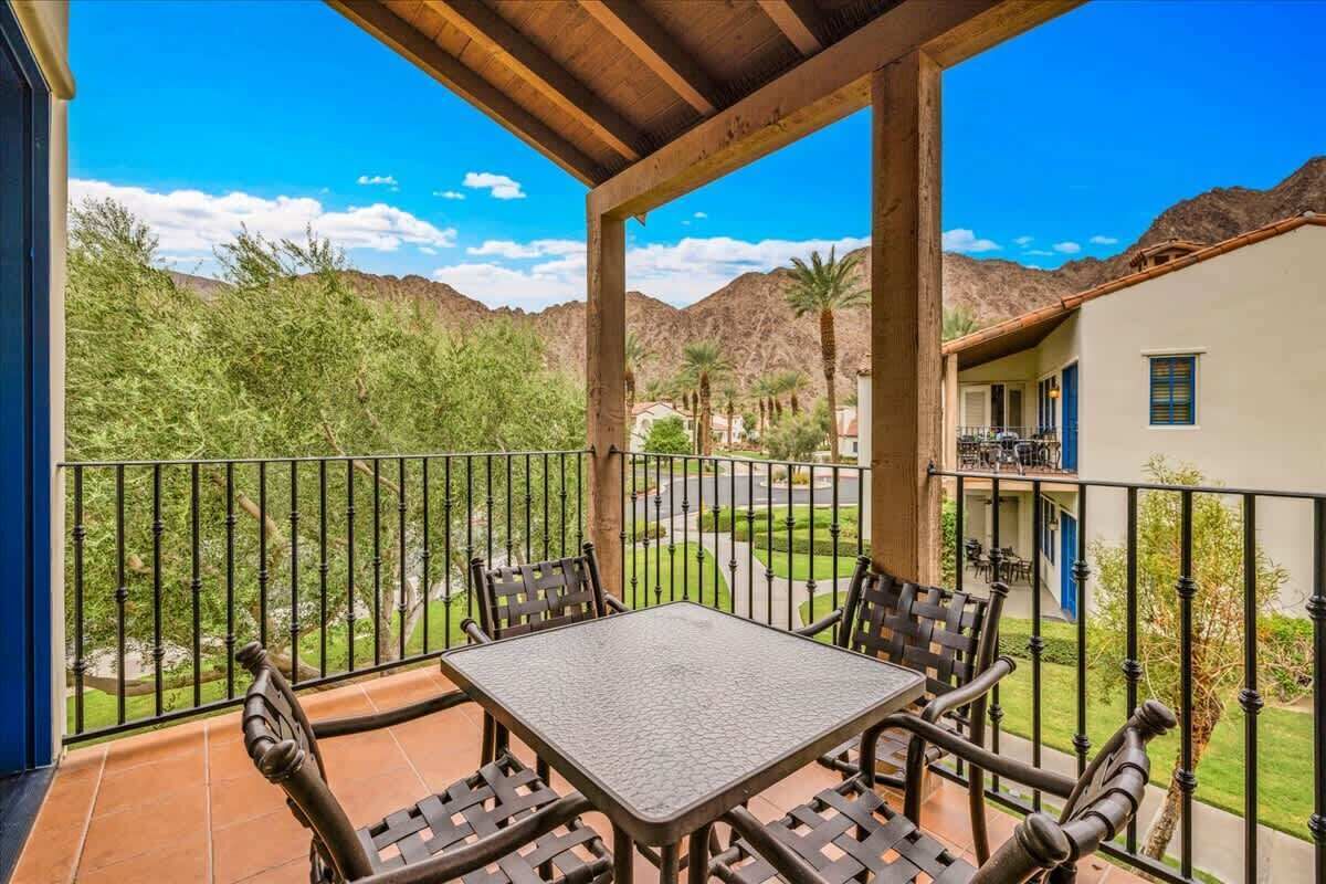 A covered patio with a table and chairs, overlooking a landscaped garden and distant mountains.