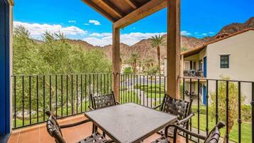 A covered patio with a table and chairs, overlooking a landscaped garden and distant mountains.