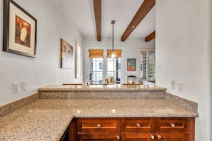 A kitchen with granite countertops, wooden cabinets, and a pendant light. - Desert Sky Vista A | 1BR Legacy Villa (La Quinta)