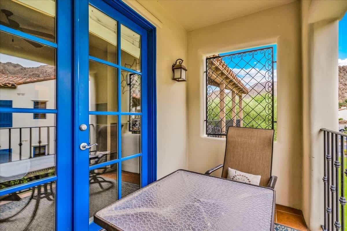 A room with a blue door, a small table, a chair, and a window with a view of a building and mountains.