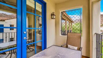 A room with a blue door, a small table, a chair, and a window with a view of a building and mountains.