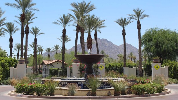 A landscaped area with a central fountain, palm trees, and a mountain in the background. - Desert Sky Vista C | Studio Legacy Villa (La Quinta)