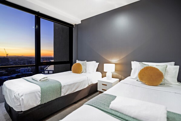 Ein Hotelzimmer mit zwei Betten, einem Nachttisch und einem großen Fenster mit Blick auf die Stadt.